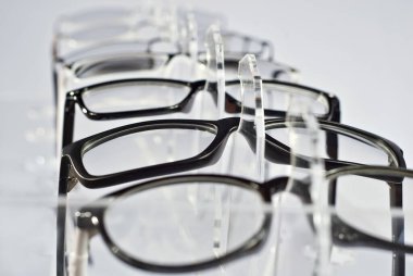 Beyaz arka planda bir sürü bardak var. Bardaklar şeffaf bir vitrinde üst üste dizilmiş. Cam, gri masanın üzerinde duruyor. İndirim ve optik sergi.