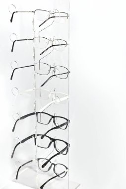 Beyaz arka planda bir sürü bardak var. Bardaklar şeffaf bir vitrinde üst üste dizilmiş. Cam, gri masanın üzerinde duruyor. İndirim ve optik sergi.