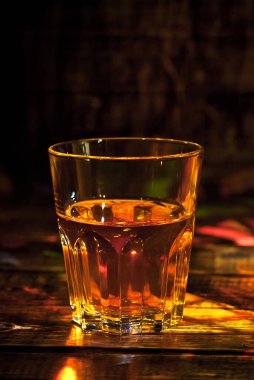 Şişenin yanında bir bardak alkol. Siyah ahşap bir masada viski. Karanlık arka planda içkiler bulanık.