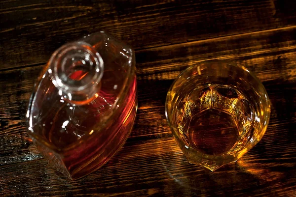 A glass of alcohol near a bottle. Old whiskey bottle on black wooden table. Drinks on a dark blurred background.