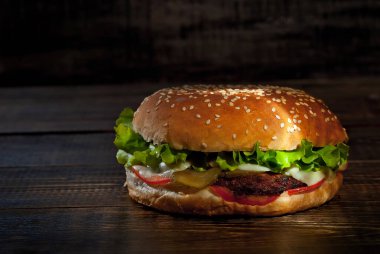 Koyu ahşap bir tahtanın üzerinde hamburger. Siyah arka planda pirzola ve bitkilerle çizburger. Çelişkili çarpıcı ışığı olan yemekler. Bun yakın plan..