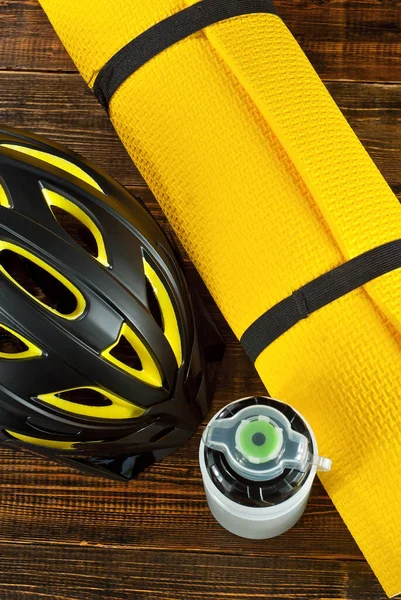 Bicycle helmet, yoga mat and water bottle on a black background. Accessories for active recreation on a brown shabby board.