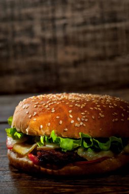 Koyu ahşap bir tahtanın üzerinde hamburger. Siyah arka planda pirzola ve bitkilerle çizburger. Çelişkili çarpıcı ışığı olan yemekler. Bun yakın plan..
