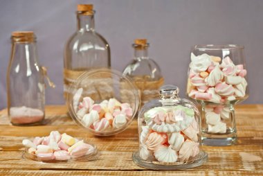 Tahta bir masada, bardaktaki şekerler. Eski püskü bir tahta üzerinde şeffaf mutfak aletleri ve marşmelovlar. Beyaz yumuşak şekerli pembe. Mor arkaplanda tatlılar.