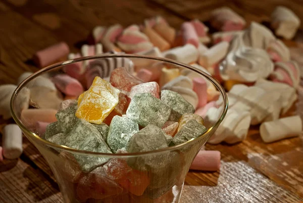 Ahşap arka planda cam bir kavanozda bir sürü tatlı var. Sütlü şekerle yakın çekim. Rahat Türk lokumu, bizet ve marşmelov pembe, eski püskü bir tahta üzerinde.