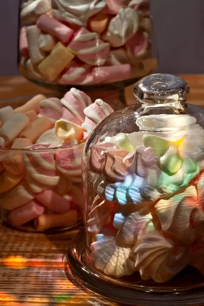 Sweets in a glass on a wooden table. Transparent utensils with marshmallows and biz on a shabby old board. Pink with white soft candies. Sweets on a purple background.
