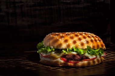 Koyu ahşap bir tahtanın üzerinde hamburger. Siyah arka planda pirzola ve bitkilerle çizburger. Çelişkili çarpıcı ışığı olan yemekler. Bun yakın plan..