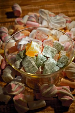 Tahta bir masada, bardaktaki şekerler. Eski püskü bir tahta üzerinde şeffaf mutfak aletleri ve marşmelovlar. Beyaz yumuşak şekerli pembe yakın çekim.