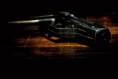 Kahverengi bir masada eski püskü bir silah. Tahtada siyah bir silah var. Yaklaş. Çelişkili dramatik ışık ile karanlık bir arkaplanda silah.