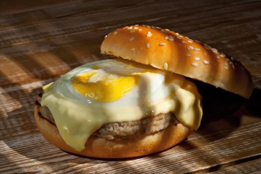 Pembe ahşap arka planda yumurtalı çizburger. Çarpıcı ışığı olan bir burger. Eski püskü tahtalardan yapılmış bir masa..