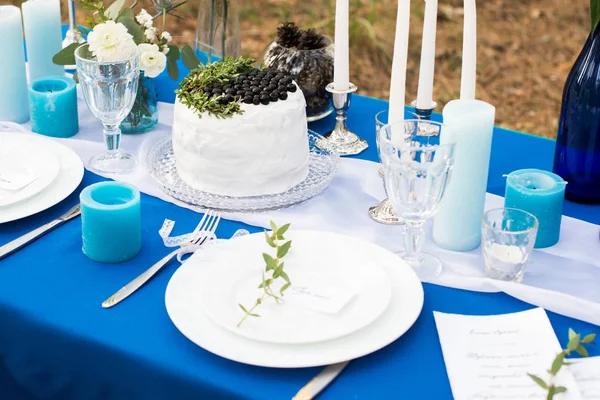 Mesa de banquete de casamento decorada com bolo, talheres com talheres e velas em uma toalha de mesa azul . — Fotografia de Stock
