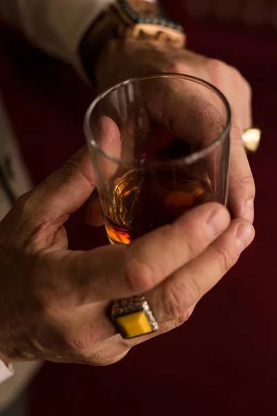 Mão de homem elegante com um anel no dedo mindinho e um copo de uísque na mão — Fotografia de Stock