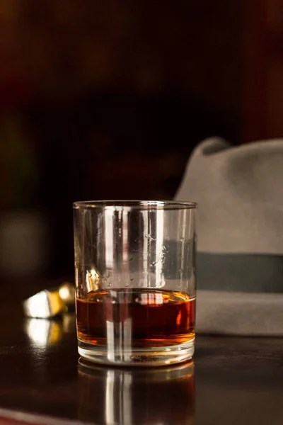 Glass of whiskey and men's hat on the wooden table — Stock Photo, Image