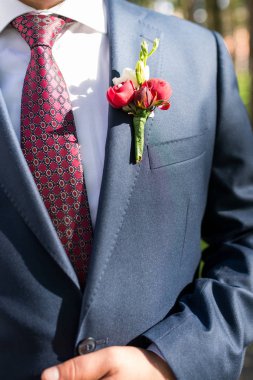 Mavi ceket, beyaz gömlek ve kırmızı kravat yaka çiçeği ile şık damat