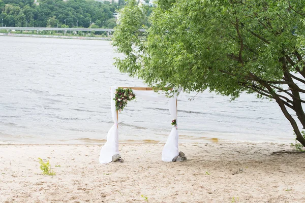 Un arco de bodas en la orilla del río con vegetación, peonías y material blanco . —  Fotos de Stock