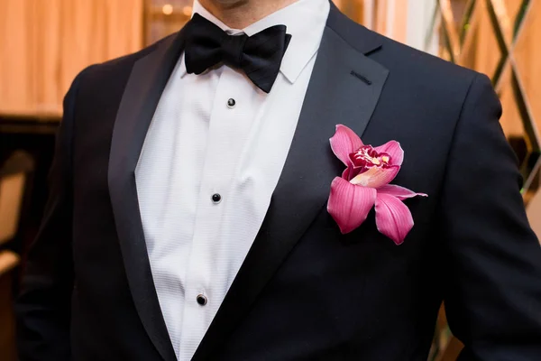 Κομψό γαμπρό σε μαύρο σακάκι, άσπρο πουκάμισο και μαύρη γραβάτα με μπουτονιέρα με ορχιδέα — Φωτογραφία Αρχείου