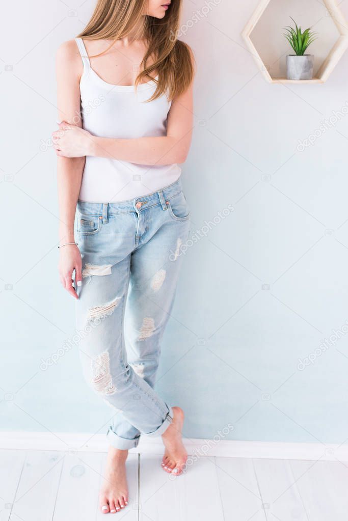 Young girl with long brown hair in blue jeans and white singlet. Fashion girl posing in jeans in the studio. Sexy woman wearing denim with holes. 