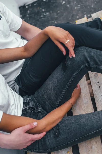 Young happy couple sitting outside a cafe on the street on the floor. Close-up of jeans on legs model. Royalty Free Stock Images