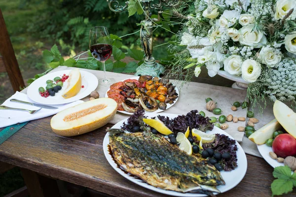 Served table with grilled vegetables and fish, glass of red wine and fruits — Stock Photo, Image