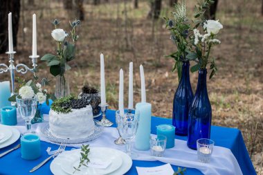 Düğün Ziyafet tablo. Beyaz kremalı pasta yabanmersini ve yeşilliklerle süslenmiş. Çatal bıçak takımı stemware levhaları ve mum üzerinde mavi bir masa örtüsü.