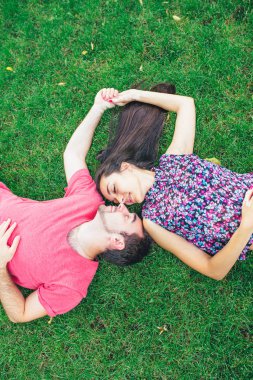 Çift yeşil çimenlerin üzerinde rahatlatıcı mutlu gülümseyerek. Genç çift açık çim üzerinde yalan güneşli yaz günü eğlenmek.