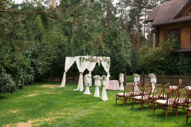 Açık havada düğün töreni için güzel platform: yeşil çimen, taze çiçeklerle süslenmiş kare kemer üzerinde ahşap sandalye