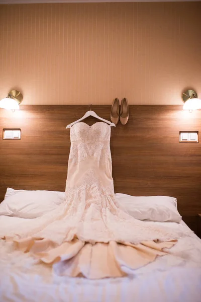Wedding dress hanging on the wall in the room and bridal biege shoes.