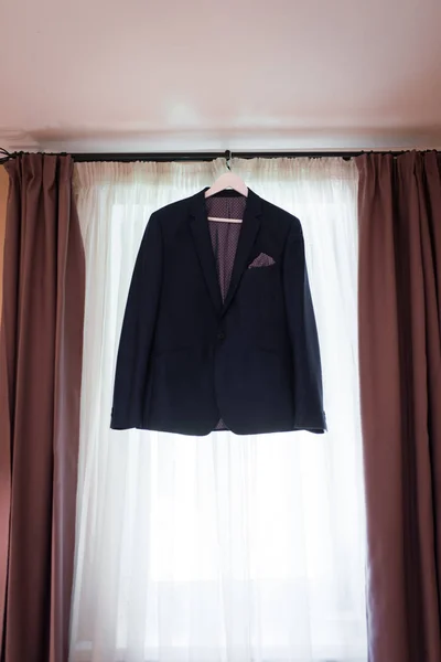 Beautiful blue groom\'s jacket hanging on the window for morning wedding preparation. Grooms accessories