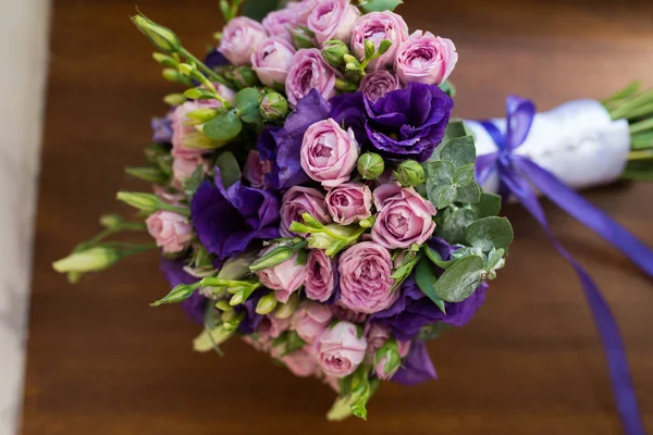 Wedding bouquet with purple and pink roses, violet flowers lying on a wooden windowsill