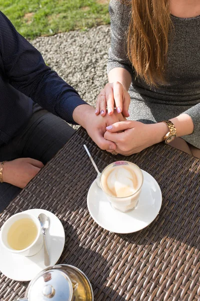 Close up of romantic couple in love holding each other hands. Close-up of couple hands on restaurant table with a glass of coffee. Romantic couple holding each other\'s hand at dinner in a luxury restaurant. Marriage proposal and engagement concept.