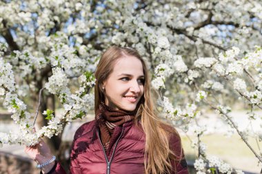 Uzun saçlı ve kahverengi bir eşarp ile güzel bir genç kız çiçek açması elma ağacı boynuna sarılır. Bahar