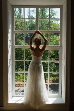 Gelin gelin sabah arka kapağı transparan, romantik atmosferini tür. Güzel genç gelin beyaz gelinlik kapalı. Lüks modeli ayakta büyük pencere karşı.