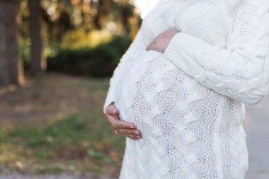 Hamile bir kadın elleriyle karnına dokunuyor.