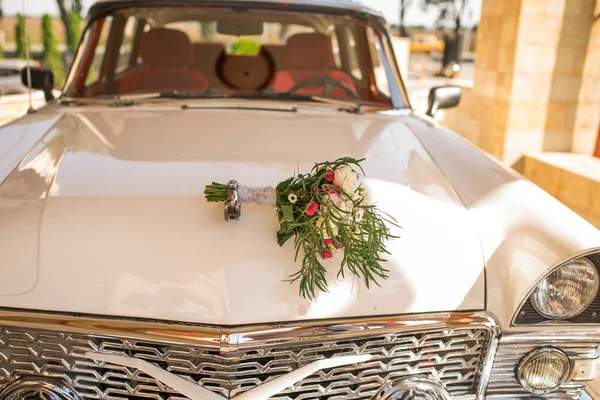 新郎新婦の白い車のボンネットの上に横になっている緑の多い白とピンクの花と緑豊かなブライダル ブーケ — ストック写真