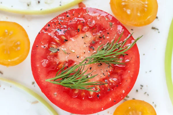 Round juicy slice of red tomato with herbs de Provence, sea salt and slices of yellow tomatoes.