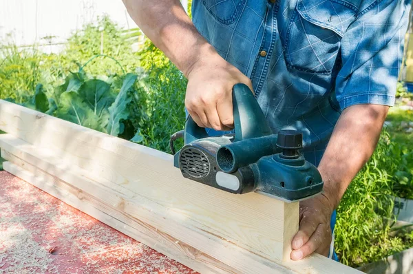 The master sharpens the wooden panel with an electric sander on a Sunny day in the garden.