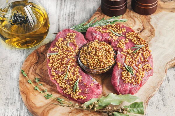 Cuts of beef for grilling on a cutting Board olive wood with pickled Dijon mustard, rosemary and herbs de Provence in a rustic style.
