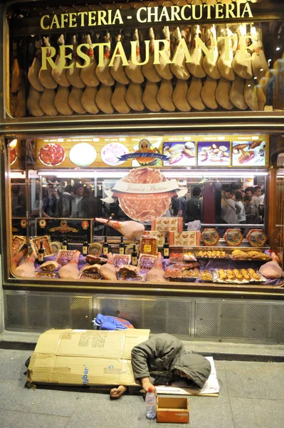 Sovande hemlösa mannen på en trottoar nära café i centrala Madrid. — Stockfoto