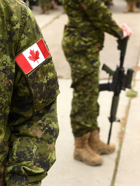 Bandeira do Canadá no uniforme militar e soldado com arma em segundo plano . — Fotografia de Stock