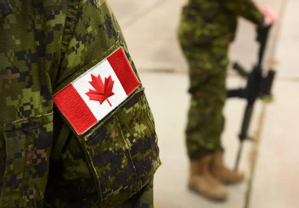 군복을 입고 뒤에 무기를 든 군인이서 있는 캐나다 국기. — 스톡 사진