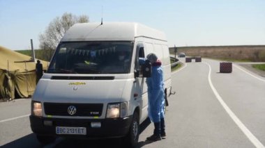 Lviv, Ukrayna - 10 Nisan 2020: Bir tıp çalışanı Ukrayna 'nın Lviv bölgesinin girişindeki bir kontrol noktasında bir sürücünün sıcaklığını kontrol eder. Koronavirüs COVID-19 salgını nedeniyle Ukrayna 'daki karantina kısıtlamaları. 
