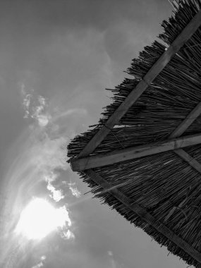 Sahilde gökyüzüne karşı duran kamış plajı şemsiyelerinin siyah ve beyaz fotoğrafları.