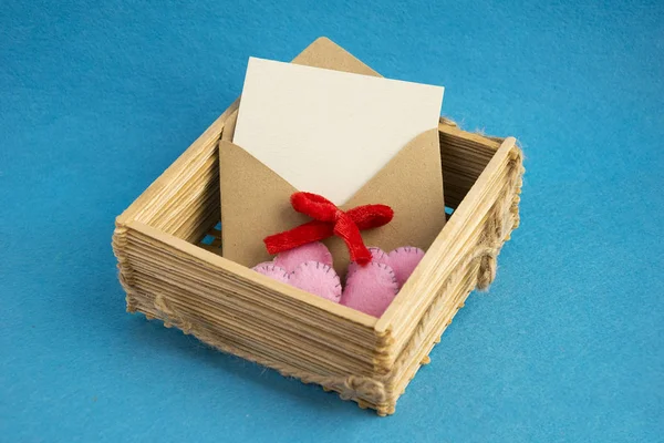 Uitnodiging envelop in houten rieten mand versierd met roze harten geïsoleerd op blauwe achtergrond. — Stockfoto
