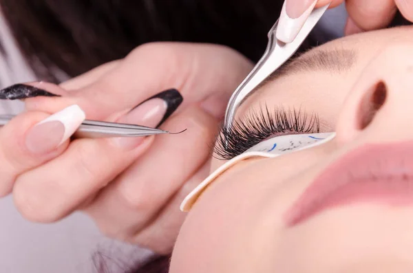 Beautiful young woman or teenager extends eyelashes in salon — Stock Photo, Image