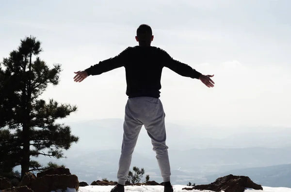 man in a track suit stands high on the mountain and exercise in