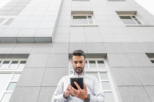 Businessman use digital tablet in front of large office building