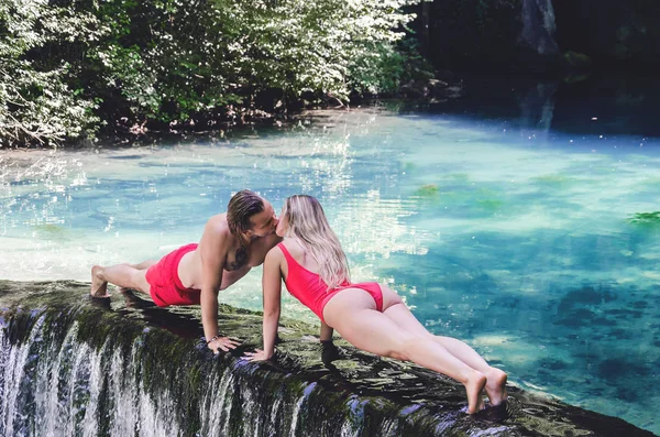 Casal de biquíni fazendo empurrar para cima sobre cachoeira — Fotografia de Stock