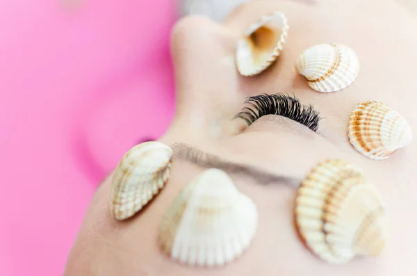 close-up of woman face with excellent eyelashes and seashells. Upgrading or extension your eyelashes before going to the sea