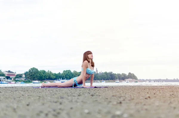 Joven chica haciendo cobra pose en yoga en la playa al aire libre — Foto de Stock