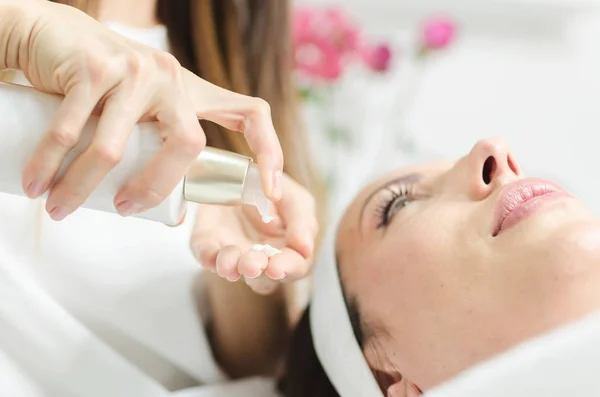 female applying cream lotion in hand from a bottle and put on female client face to finish skin treatment.